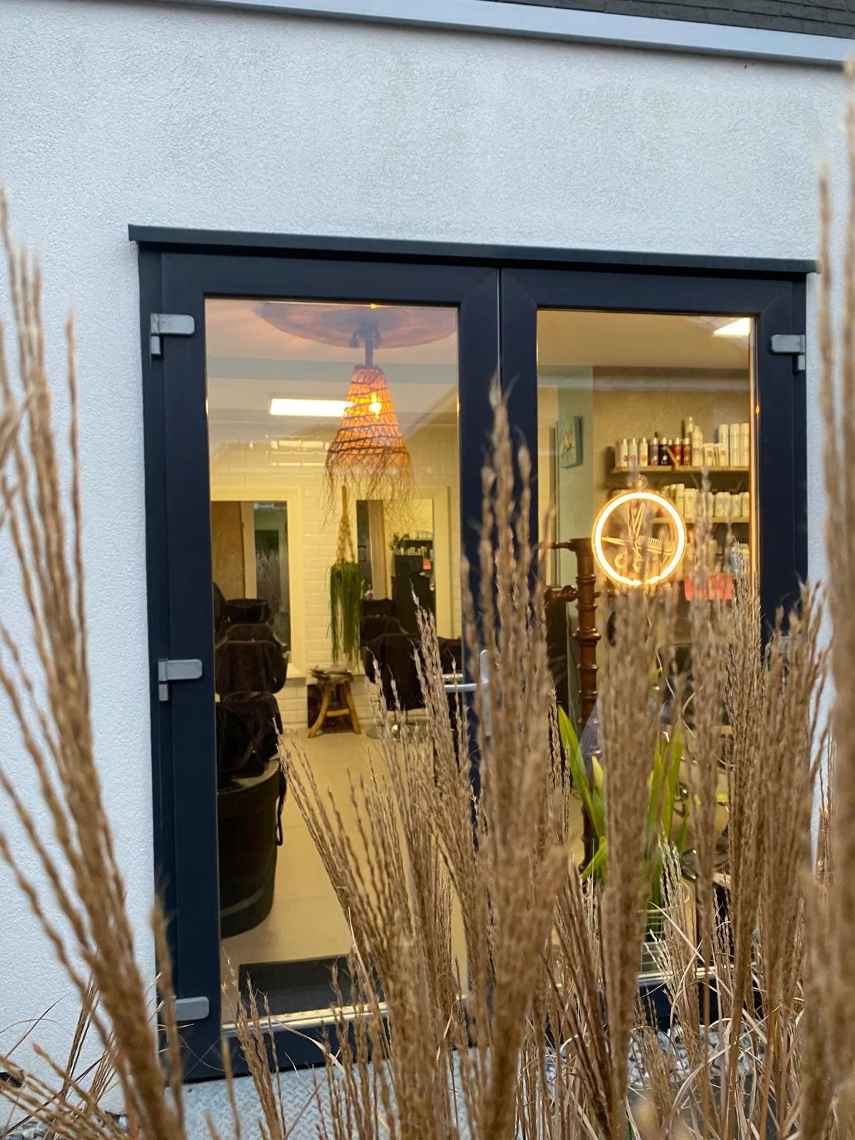 Door de openslaande deuren zie je de salon: een rieten hanglamp, een lichtgevend schaarteken en pluimgras op de voorgrond